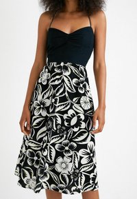 Top negro con tirantes de espagueti que se transforma en una falda floral en blanco y negro. El diseño presenta grandes flores y hojas con una textura suave.