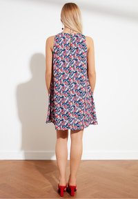 Blommig klänning i marinblått med rosa och vita mönster. Ärmlös design, knälång, med nyckelhålsdetalj bak. Röda högklackade skor fulländar looken.