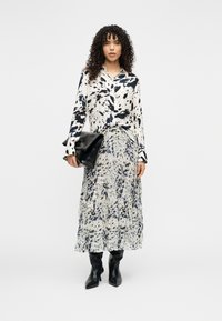 Ασπρόμαυρη μπλούζα με αφηρημένο σχέδιο, μακριά μανίκια, σετ με μια ροή, πολυεπίπεδη φούστα σε παρόμοια χρώματα και μαύρες μπότες μέχρι το γόνατο.