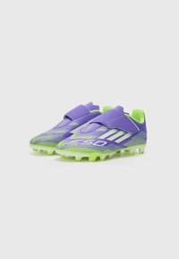 Scarpini da calcio viola e verdi con superficie texturizzata, cinturino in velcro e tacchetti moldati per la trazione. Presentano grafiche audaci e un design elegante.