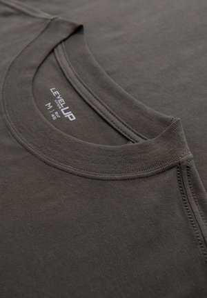 Gros plan d'un T-shirt gris foncé à col rond montrant le col côtelé, la couture d'épaule et l'étiquette imprimée de la taille et de la marque à l'intérieur de l'encolure.