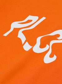 Pomarańczowa bawełniana tkanina z białym, falistym napisem. Projekt kontrastuje wyraźnie z żywym tłem, tworząc odważny element wizualny.