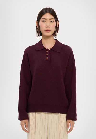 Suéter de punto burdeos con cuello tipo polo, tapeta de tres botones y un corte holgado con mangas largas. Detalle de tela texturizada visible.