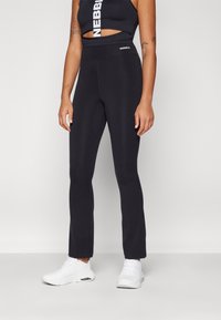 Black high-waisted leggings in a smooth, stretchy material, featuring a logo at the waistband, styled with white sneakers.