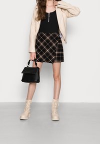 Béžová bundička z umělé kůže, černý top na ramínka, sukně mini v tmavých károvaných tónech, černá kabelka se zkrouceným uchy a béžové kotníkové boty na šněrování.