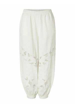 Hvite løse bukser med elastisk midjebånd og mansjetter, med blomsterinspirerte blondeutskjæringer på framsiden av bena.