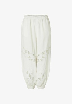 Hvite løse bukser med elastisk midjebånd og mansjetter, med blomsterinspirerte blondeutskjæringer på framsiden av bena.