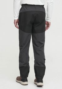 Pantalones de exterior para hombre en negro con una cinturilla flexible, tejido impermeable y secciones de rodilla reforzadas. Presenta cierres a presión en los tobillos.