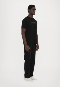 Schwarzes T-Shirt mit kurzen Ärmeln und einem bedruckten Design. Kombiniert mit schwarzen Hosen und hellen Sneakers. Schlichter und figurbetonter Stil.