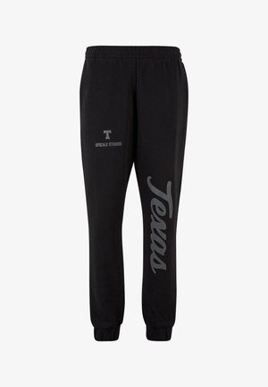 Čierne tepláky vyrobené z bavlnenej zmesi, s šedým potlačou "Texas" na jednej nohe a logom "UPGRADE STUDIOS" na druhej strane, s elastickými manžetami.