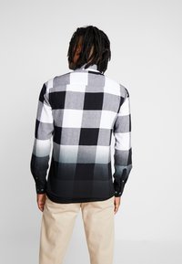 Schwarz-weiß kariertes Hemd mit langen Ärmeln und Farbverlauf von Grau zu Schwarz am Saum. Strukturierter Stoff, geknöpfte Manschetten und Kragen.