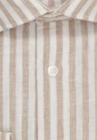 Camicia leggera in tessuto intrecciato con righe verticali beige e bianche. Presenta un colletto classico e un bottone bianco sul collo.