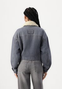Kurt denimhjakke med vertikale pinstriper, lys grå krage og ryggmerke. Kombinert med høyt liv grå jeans.