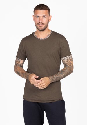 Camiseta de manga corta verde oliva con cuello redondo, textura suave y corte relajado, combinada con pantalones azul marino.