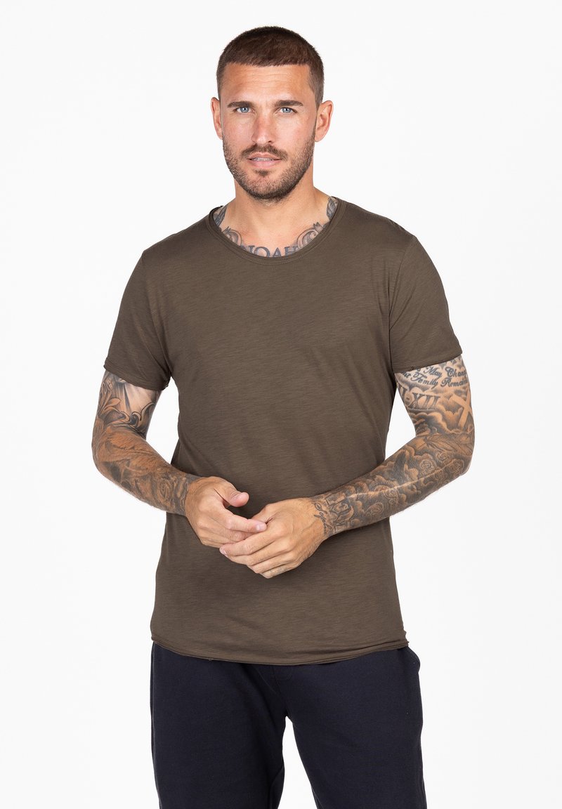 T-shirt verde oliva a maniche corte con colletto rotondo, texture liscia e vestibilità rilassata, indossato con pantaloni blu navy.