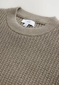 Suéter de punto beige con textura acanalada, cuello redondo y etiqueta visible con la marca "NEXT," talla M.