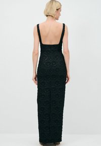 Schwarzes Spitzenkleid mit rundem Rückenausschnitt, taillierter Silhouette, floraler Textur und einem subtilen Schlitz am Saum für einen leichteren Bewegungsablauf.