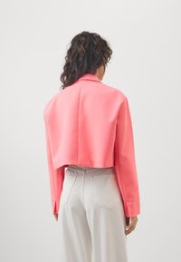 Giacca accorciata in tessuto rosa brillante, con colletto con alette, maniche lunghe e texture liscia. Design minimalista con linee pulite.