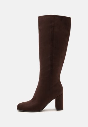 Botte haute en daim brun foncé jusqu'au genou avec talon bloc et bout rond, montrée de côté sur un fond clair.