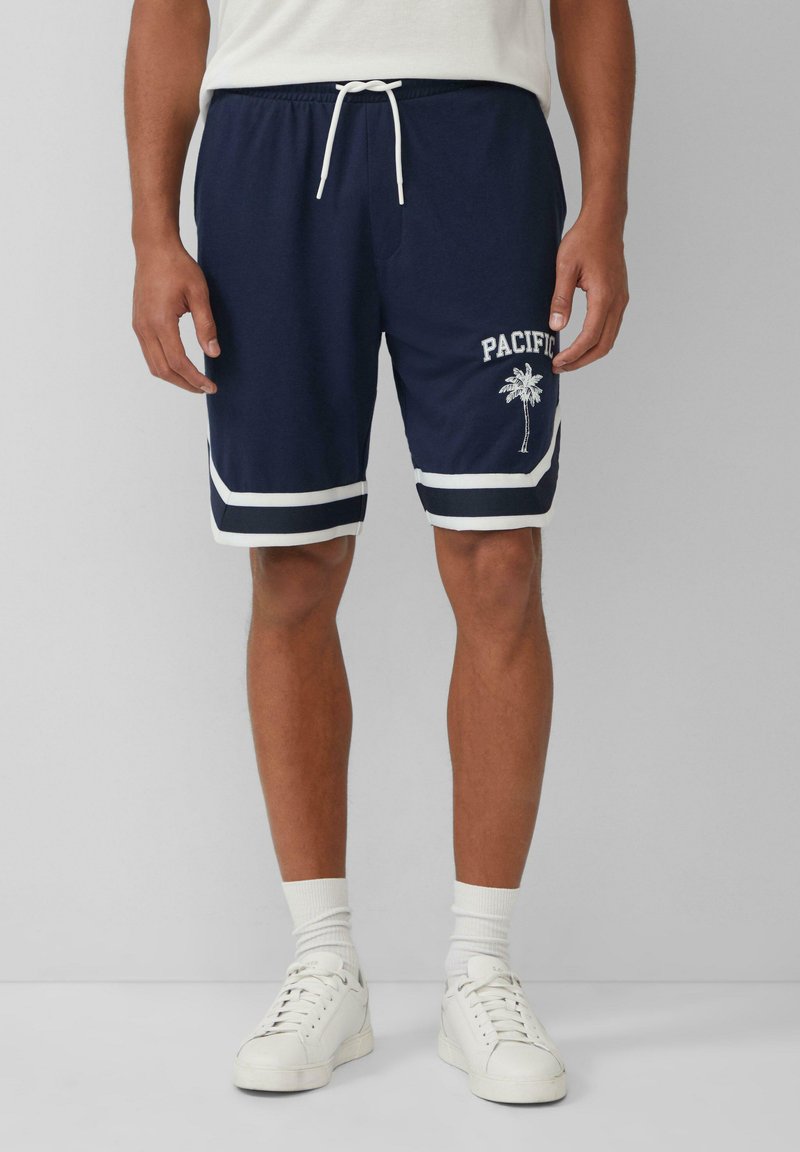 Marineblauwe shorts met witte strepen aan de zoom, elastische tailleband en het ontwerp "PACIFIC" met een palmboom op het linkerpootje. Van katoenmateriaal.