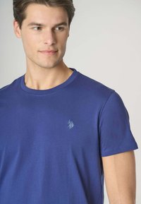 T-shirt in cotone blu navy con collo rotondo e maniche corte, caratterizzato da un piccolo logo ricamato sul lato sinistro del petto. Texture liscia.