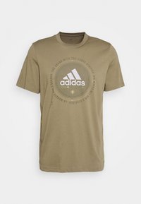 Olivenfarvet bomulds t-shirt med rund halsudskæring, korte ærmer og et grafisk tryk med Adidas-logoet i hvid.