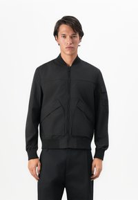 Black bomber jacket made of smooth fabric. Features a front zipper, ribbed cuffs, and two angled side pockets. Minimalist design.