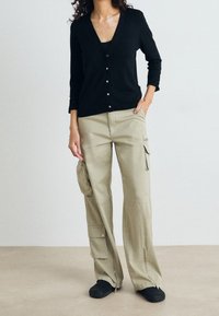 Svart knappad cardigan med V-ringning och långa ärmar, kombinerad med löst sittande olivgröna cargobyxor med sidofickor och dragkedjor.