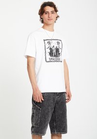 White cotton t-shirt featuring a black graphic print in a rectangular design. Paired with knee-length dark denim shorts with a side pocket.