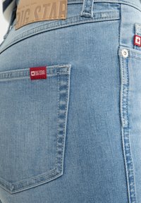 Svetle modré džíny z denimu s červenou a bílou nášivkou na zadní kapse, s čistým prošíváním a hladkým povrchem.