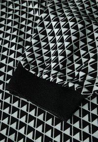 Tessuto nero e grigio chiaro con un motivo geometrico a triangoli, caratterizzato da una superficie texturizzata e un polsino nero a coste.