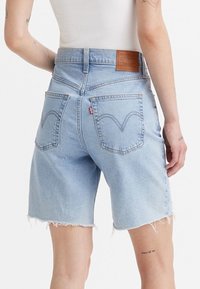 Světle modré džíny šortky s třepeným lemem, vysokým pasem a výraznými zadními kapsami se švy a štítkem značky.