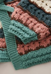 Cardigan croșetat cu modele texturate în verde-teal închis, roz, crem și maro. Prezintă manșete rib și închidere cu șnur.