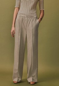 Pantaloni bej deschis, cu croi larg, cu o textură strălucitoare, având un elastic la talie, pliuri frontale și buzunare laterale. Pot fi asortați cu un top apoiat cu dungi.