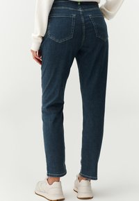 Blue denim jeans with a straight cut, visible stitching, five-pocket design, and a mid-rise waist, paired with white sneakers.