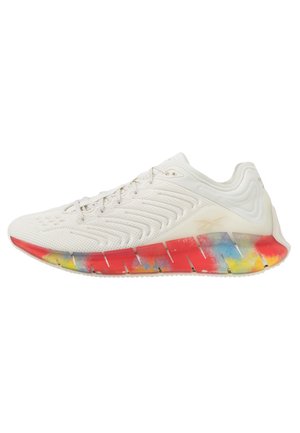 Chaussure de sport blanche avec tige texturée et semelle segmentée multicolore rouge, jaune et bleue, vue de côté sur fond blanc.