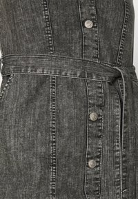 Black denim dress featuring a belted waist, silver button details, and contrasting stitching. The fabric has a slight texture and finish.