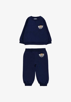 Completo in cotone blu navy composto da felpa e pantaloni jogger. La felpa presenta un grafiche di un orso e il nome del brand; i pantaloni jogger presentano un dettaglio coordinato dell'orso.