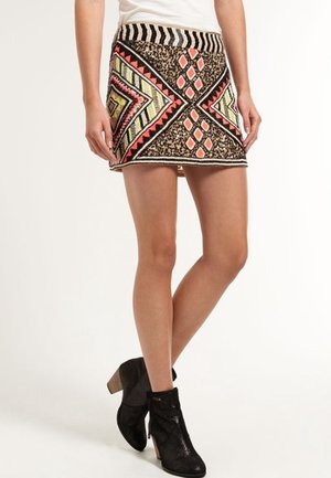 Mini spódniczka z geometrycznymi wzorami w kolorach czarnym, pomarańczowym, zielonym i beżowym, połączona z czarnymi botkami na drewnianym obcasie.