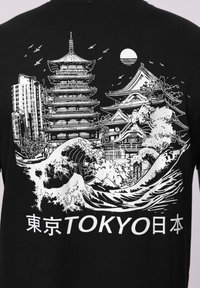 Paysage urbain de Tokyo sur un t-shirt noir avec une pagode traditionnelle, des bâtiments modernes, des vagues océaniques, des oiseaux, le soleil et du texte japonais.