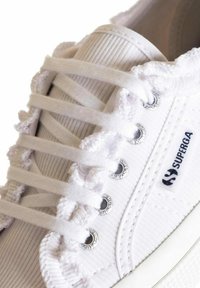 Sneaker bianco in tela con texture rigata, dotato di lacci pelosi passati attraverso occhielli argentati. Logo di lato. Design classico a basso profilo.