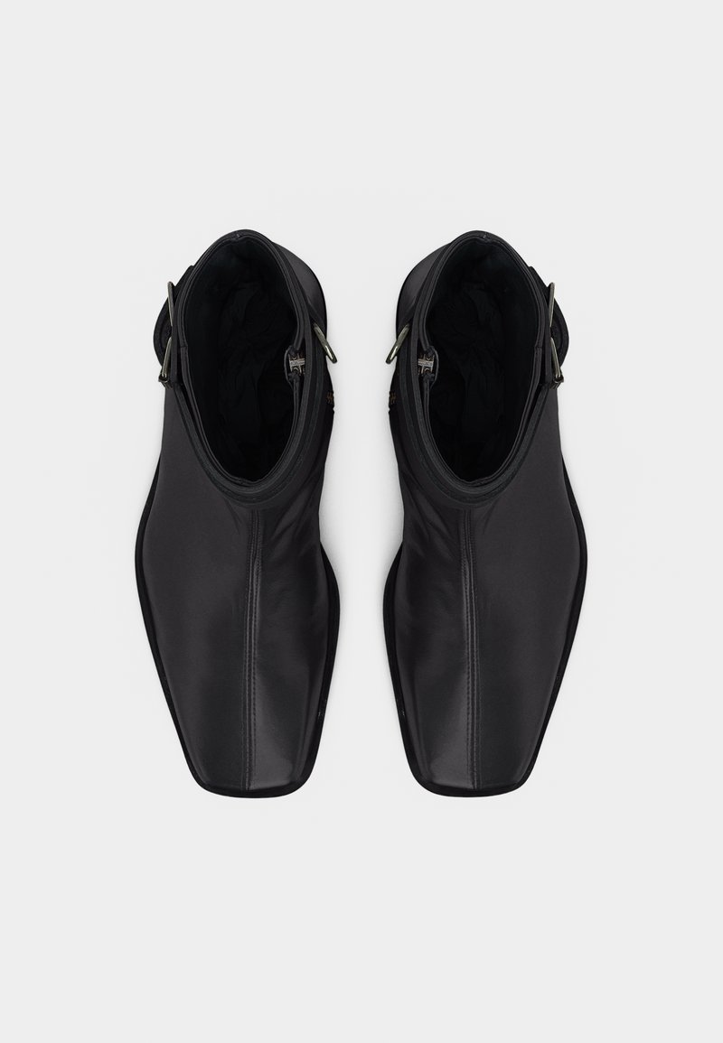 Coppia di stivaletti neri in pelle con punte quadrate e fibbie laterali color argento, visti dall'alto su sfondo bianco.