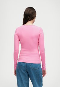 Dugih rukava, uska ružičasta majica od meke rebraste tkanine s okruglim izrezom. Uparena s labavim, svijetloplavim trapericama.
