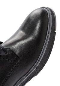 Zwarte leren schoen met een gladde afwerking, voorzien van een ronde neus, grijze rubberen zool en een eenvoudig vetersluiting ontwerp.