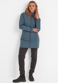 Softshell hooded coat in slate blue, featuring a full zipper, side pockets, and long sleeves, paired with dark fitted pants and ankle boots.