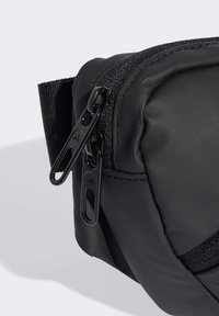 Bolsa negra de nylon con superficie texturizada, presenta cremalleras dobles negras, forma angular y costuras reforzadas a lo largo de los bordes.