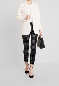Vit blazer över en plisserad topp, ihop med svarta byxor med prickar. Svarta klackar med ankelrem och en liten svart handväska fulländar looken.