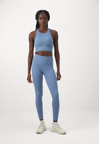 Blå ribbad atletisk crop top och matchande högmidjade leggings, tillverkade av stretchtyg, kombinerat med ljusfärgade sneakers.