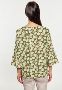 Blusa verde con motivo a foglie, maniche a campana 3/4, scollatura rotonda e chiusura posteriore con bottone. Tessuto leggero con una trama morbida.