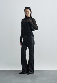 Black outfit featuring a fitted top with sheer long sleeves, paired with high-waisted black flared pants. Accessories include a small black bag.